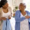 Adult daughter helping her senior mother put on a cardigan, both laughing